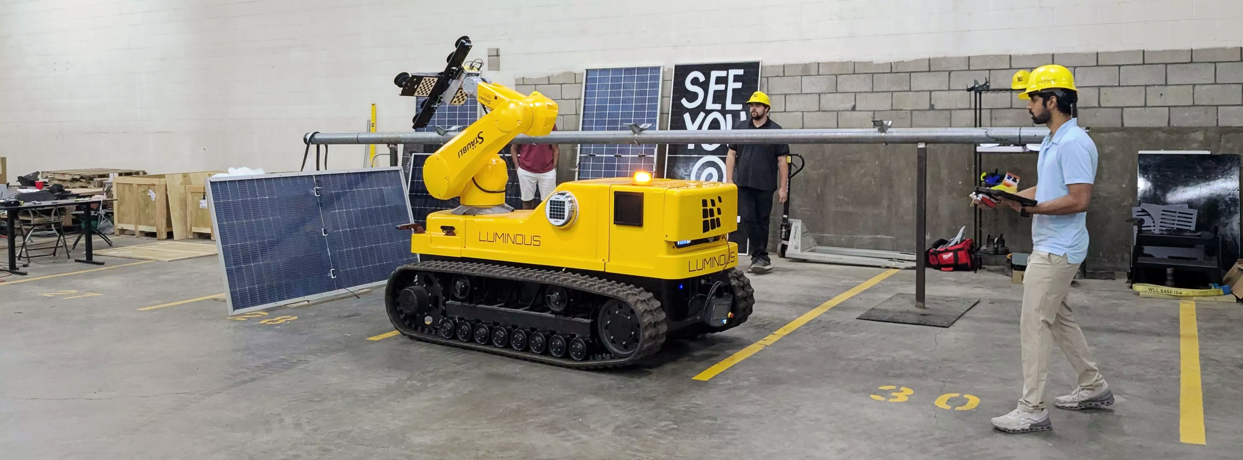 Man in hard hat controls a robotic vehicle on caterpillar treads with arm for installing solar panels