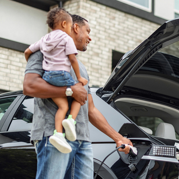 Father holding his daughter while plugging in his electric vehicle at home