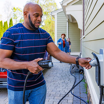 Man holding an EV charger at a home, woman and child in the background