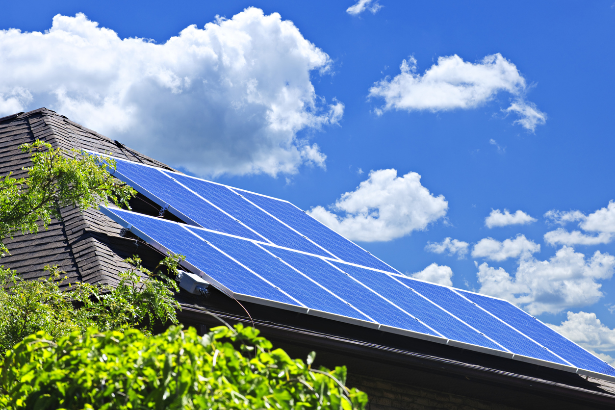 Solar panels on shingled roof under bright blue sky
