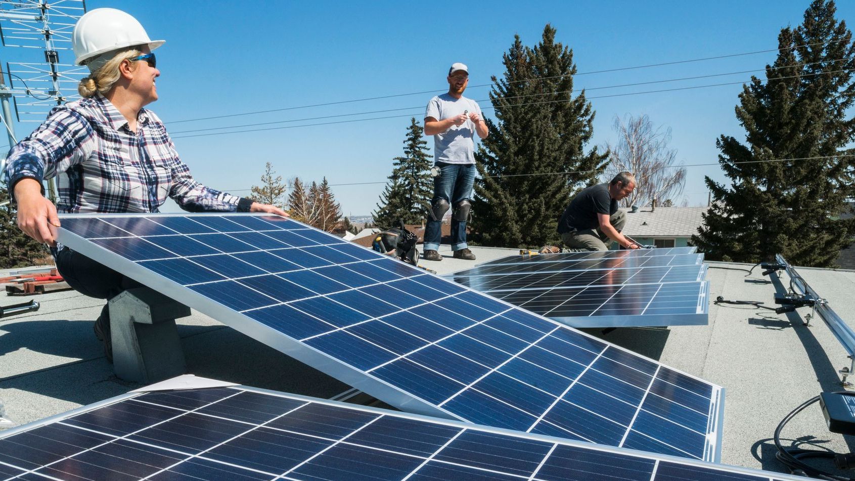 Workers installing solar panels on a residential home roof with power lines in the background