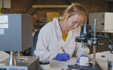 A scientist takes notes while testing paint samples in a lab.