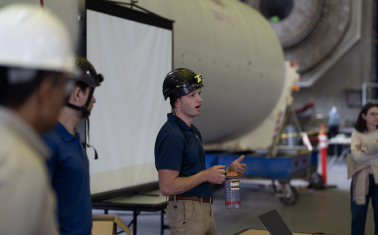 A man in a hard hat speaking to a group.