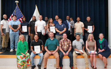 Graduates and instructors smile from a stage