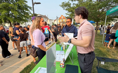 Neighbors gather at Lowell’s National Night Out 2025 community celebration. Two people talk across a table.