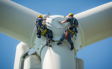 Two men, suspended from top of wind turbine performance maintenance. 