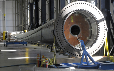 Offshore wind turbine blade lying unattached inside MassCEC’s Wind Technology Testing Center, with the circular blade root in the foreground and the blade extending across the lab floor.
