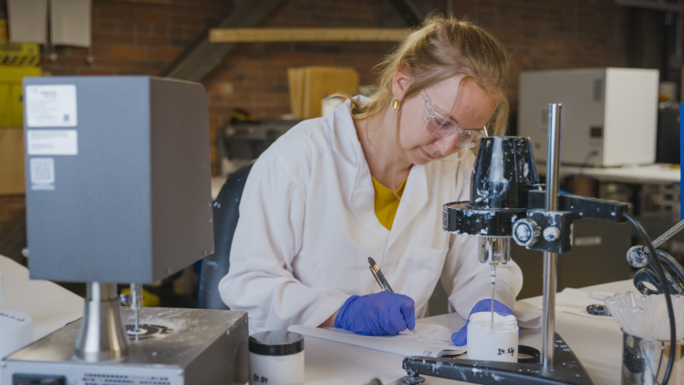 A scientist takes notes while testing paint samples in a lab.