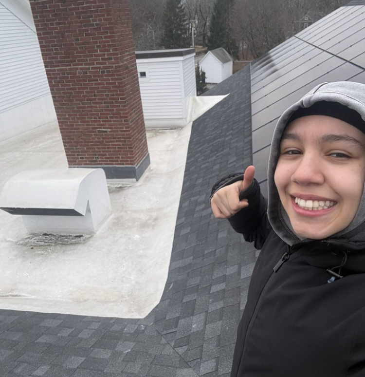 Woman standing on roof with solar panels behind her.