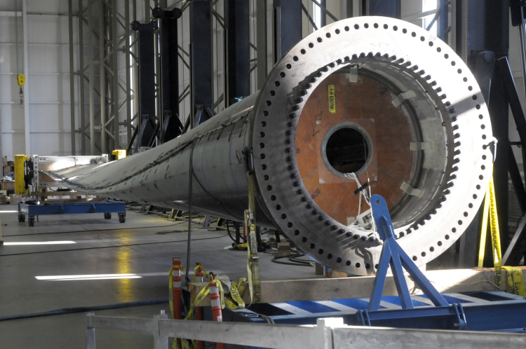 Offshore wind turbine blade lying unattached inside MassCEC’s Wind Technology Testing Center, with the circular blade root in the foreground and the blade extending across the lab floor.