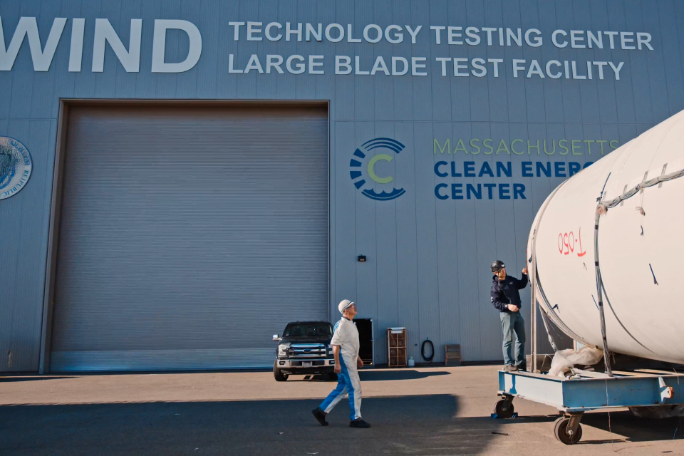 Two workers inspect a wind turbine blade outside of the Wind Technology Testing Center.