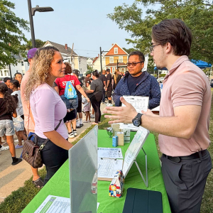 Neighbors gather at Lowell’s National Night Out 2025 community celebration. Two people talk across a table.