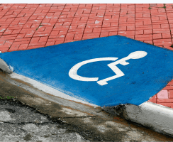Blue accessible parking curb ramp with wheelchair accessibility symbol painted on pavement.