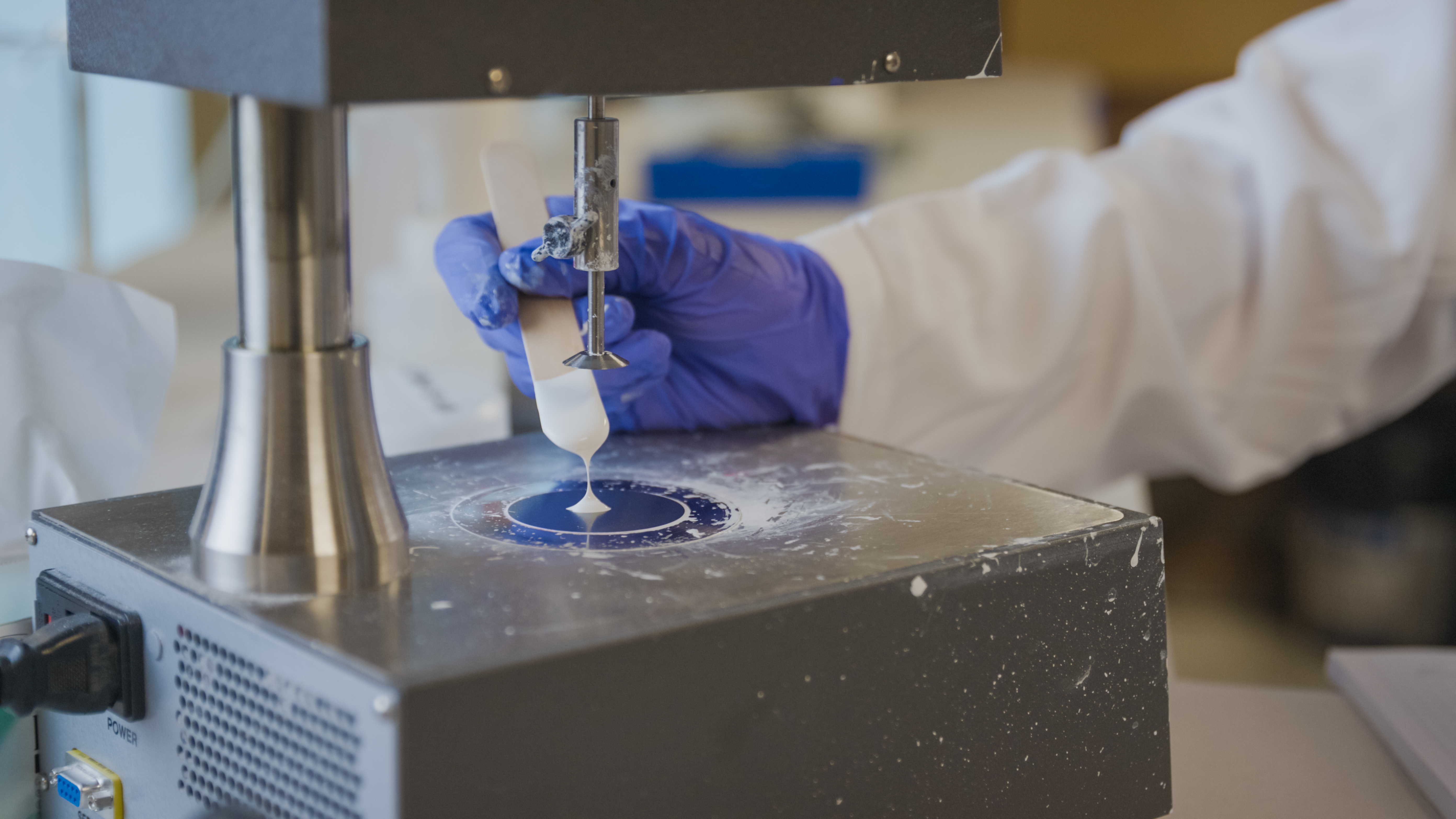 White paint on a stick being held in a lab testing device.