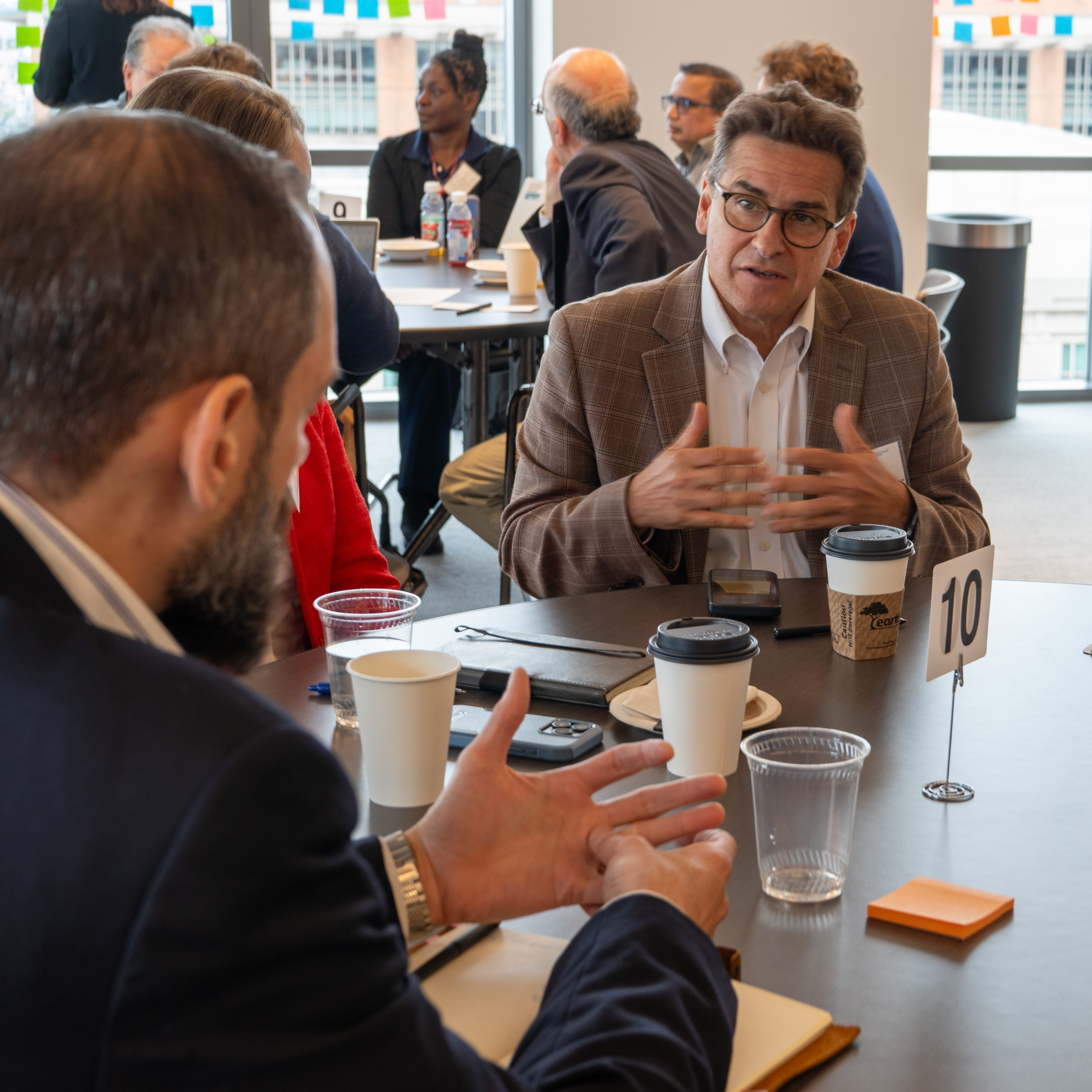Man in a suit sitting at a round table gestures to another event attendee