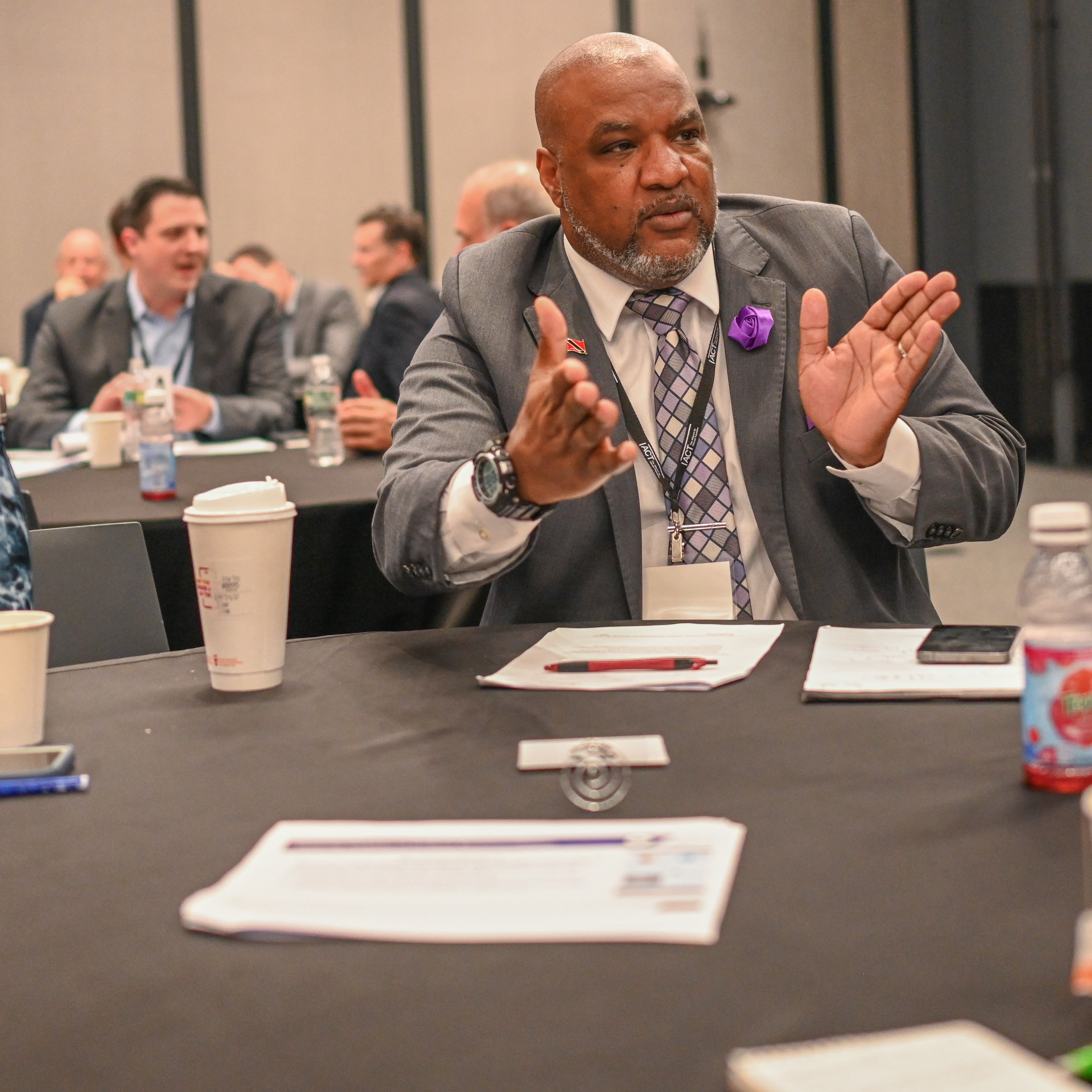 Man in a suit sitting at a round table gestures to other event participants