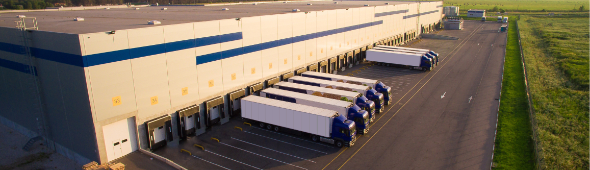 Large distribution warehouse with multiple semi trucks parked at loading dock bays.