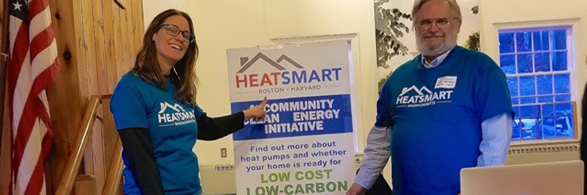 Two people pointing to Bolton-Harvard HeatSmart banner