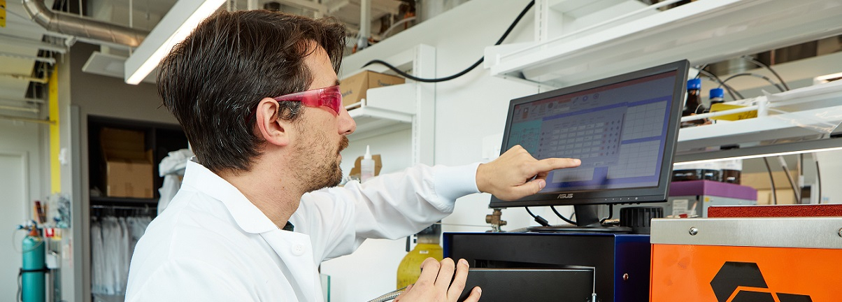 Man in lab coat and goggles working at computer