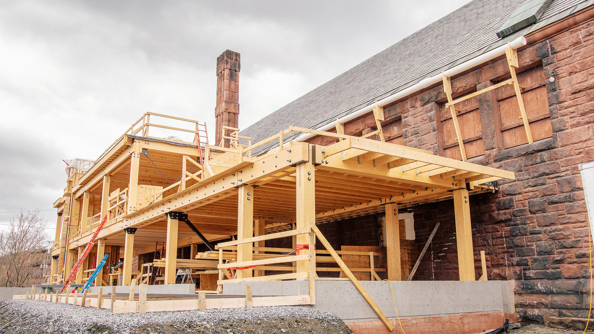 Mass timber building addition under construction featuring exposed engineered wood beams and columns attached to an existing masonry structure.